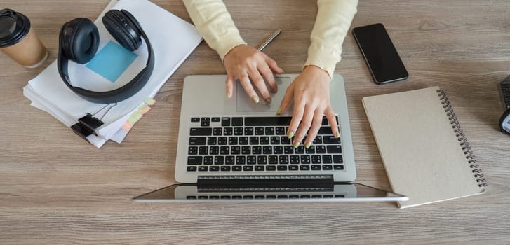 A focused view of hands typing on a laptop, with headphones and notes nearby, illustrating a productive home office environment.