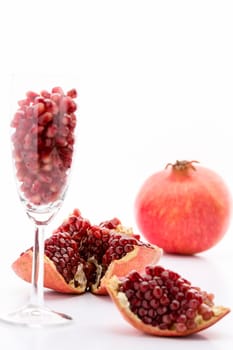 Red pomegranate seeds in a champagne glass and embedded in the reddish skin of the broken-up grenadine fruit. Behind is an entire Punica granatum..