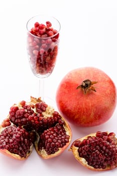 One whole pomegranate, Punica granatum. Next to it are pieces of a broken-up pomegranate. A champagne glass filled with ripe pomegranate seeds..