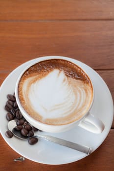 Cup of hot caffe latte with coffee grains on the wooden table