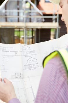Architect On Building Site Looking At Plans For House