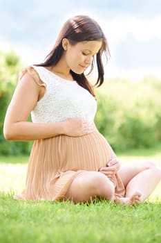 Pregnant Woman Sitting On Grass Outdoors Holding Bump