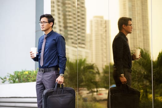 Portrait of chinese businessman standing near office building in Panama coffee cup and suitcase