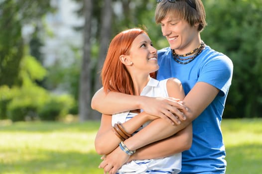 Smiling couple embracing looking at each other in sunny park
