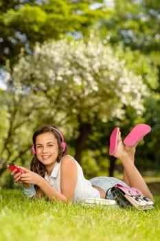 Smiling student girl lying in summer park listen to music