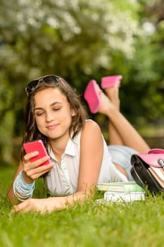 Teenage girl with pink mobile phone lying on grass summer
