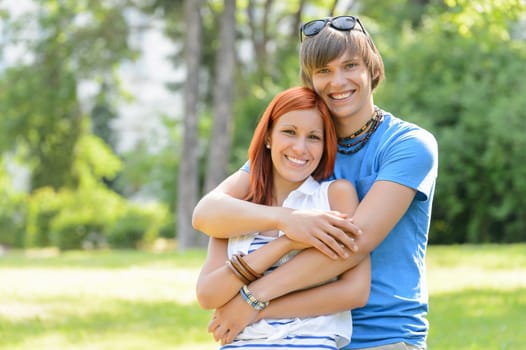 Teenage couple hugging in sunny park smiling at camera