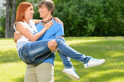 Teenage boyfriend carry girlfriend in his arms smiling in sunny park