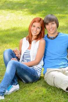 Teenage couple sitting on grass embracing in sunny park
