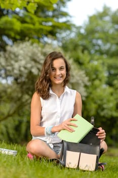 Teenage student woman sitting grass putting books in school bag