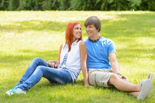 Teenage couple sitting on grass looking at each other summer