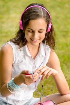 Teenage girl listening to music with headphones sitting on grass