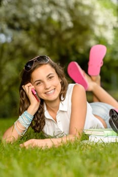 Cheerful student girl lying on grass calling mobile phone summer