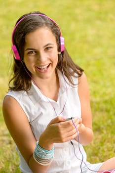 Laughing teenage girl listening to music sitting on grass summer