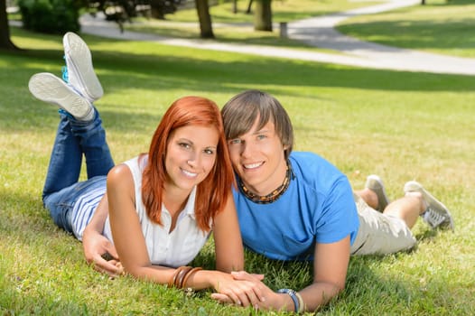 Smiling teenage couple lying in sunny park enjoy first love