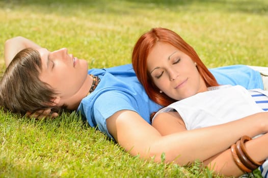 Teenage couple relaxing lying on grass closed eyes summer day