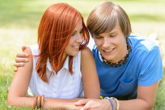 Teenage boyfriend and girlfriend holding hands lying on grass sunny