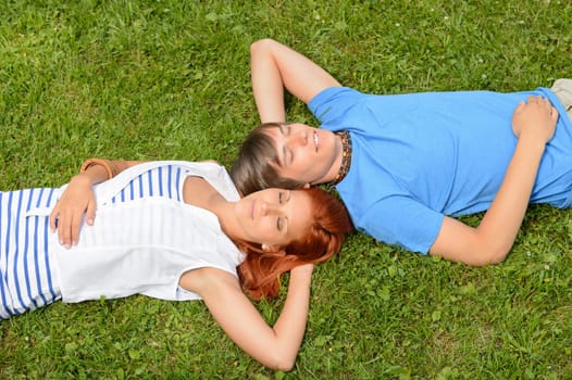 Teenage couple lying on grass relaxing closed eyes top view
