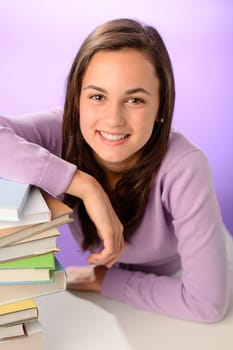 Smiling student girl with pile of books on purple background