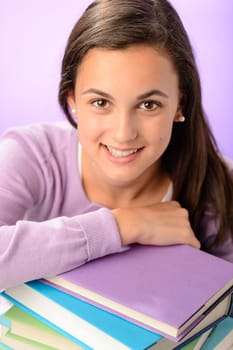 Happy student girl leaning on pile of books purple background
