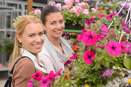 Two woman customers in garden center standing between colorful flowers