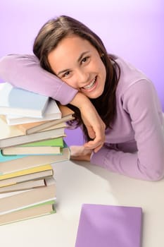 Smiling student girl resting head on stack of books purple background