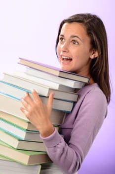 Shocked student girl carry stack of books on purple background