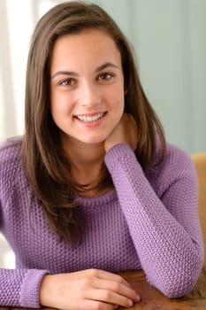 Cute teenage girl sitting behind table wear purple jumper portrait