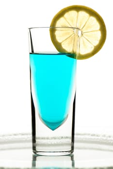 Glass with turquoise drink and lemon in the backlight