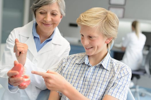 Teenage patient boy dentist woman show dentures teeth at dental surgery