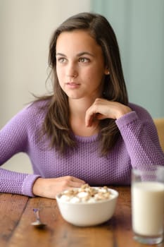 Thoughtful young woman with cereal breakfast wooden table looking aside