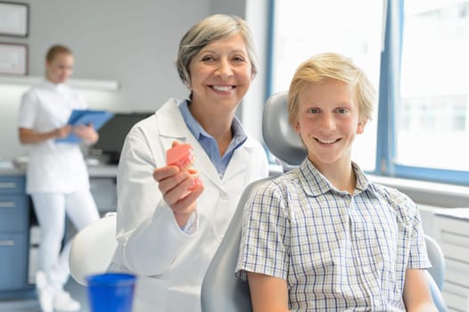 Teenager boy patient dentist hold teeth dentures dental assistant office