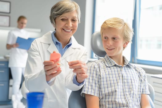 Dentist show teenage patient teeth dentures assistant at dental clinic