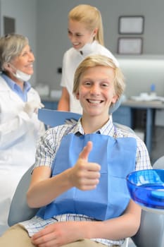 Teenager patient thumbup at dental surgery dentist and nurse background