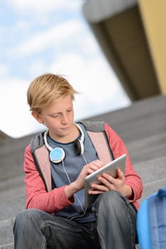 Teenage student boy using tablet sitting on steps outside school