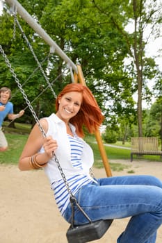 Two teenagers sitting swing in park playground laughing having fun
