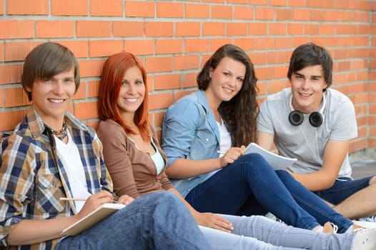 Group of friends students sitting in row against brick wall