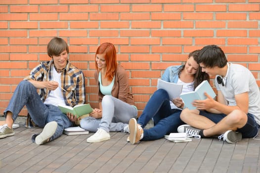 Group of students with books hanging out sitting against wall