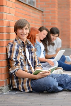 Studying boy with college friends sitting on ground outside campus