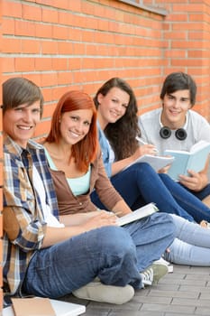 College students sitting on ground against brick wall holding books