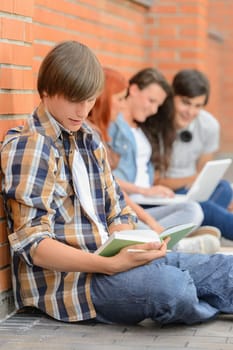 Young man studying book college friends sitting ground using laptop