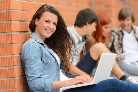Student girl sitting with laptop outside campus friends in background