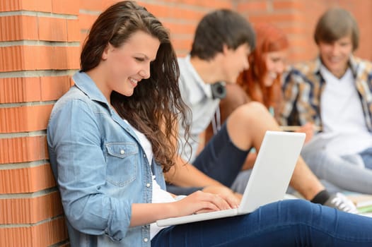 Student girl working on laptop outside college friends in background