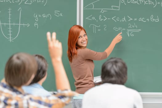 Math lesson student write on green chalkboard looking at classmates