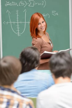 Student girl standing front of green chalkboard looking at classmates