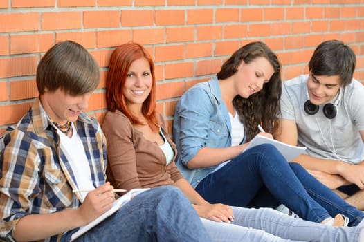 College students sitting in row against brick wall writing notes