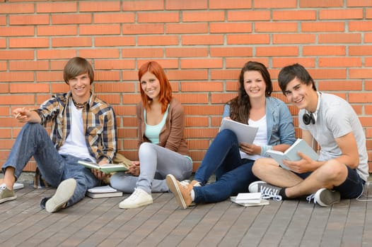 College students with books sitting ground by brick wall