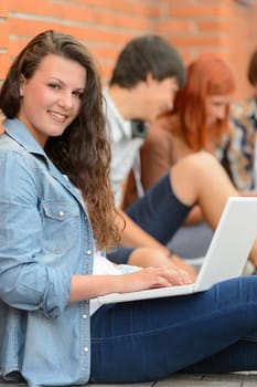 Student girl working on laptop outside college friends in background