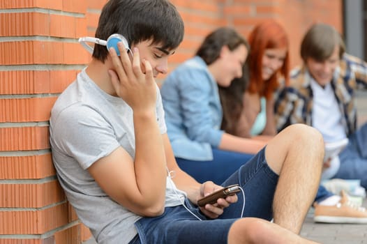 Student boy with headphones college friends sitting outside campus chatting