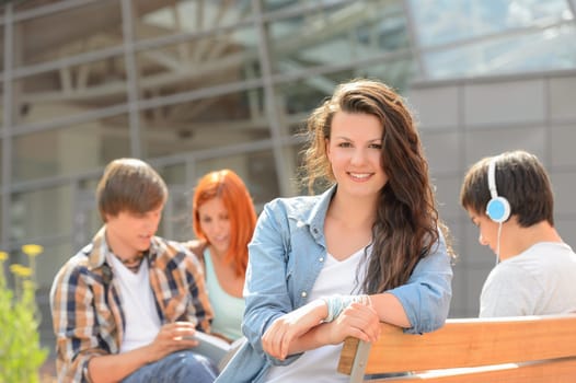 Student girl sitting on bench outside campus with friends sunny